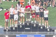 Luke Barreto, Luke Sinclair, Paul Sinclair, Daniel Mitchell, Kade Stukel, Coach Kurt Stukel, Eli Fogel, Luke Stukel, Finn Adams, and Pierce Stukel, shown l to r, stand on the winners’ podium with the school’s first ever team state championship plaque.
