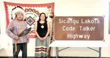 Willie Bearshield and Lisa White Pipe, descendants of Code Talker Charles White Pipe, stand next to the sign designating a 153-mile portion of US Highway 18 as Sicangu Lakota Code Talker Highway in honor of the many Lakota Code Talkers from South Dakota who served the US military in World War II.