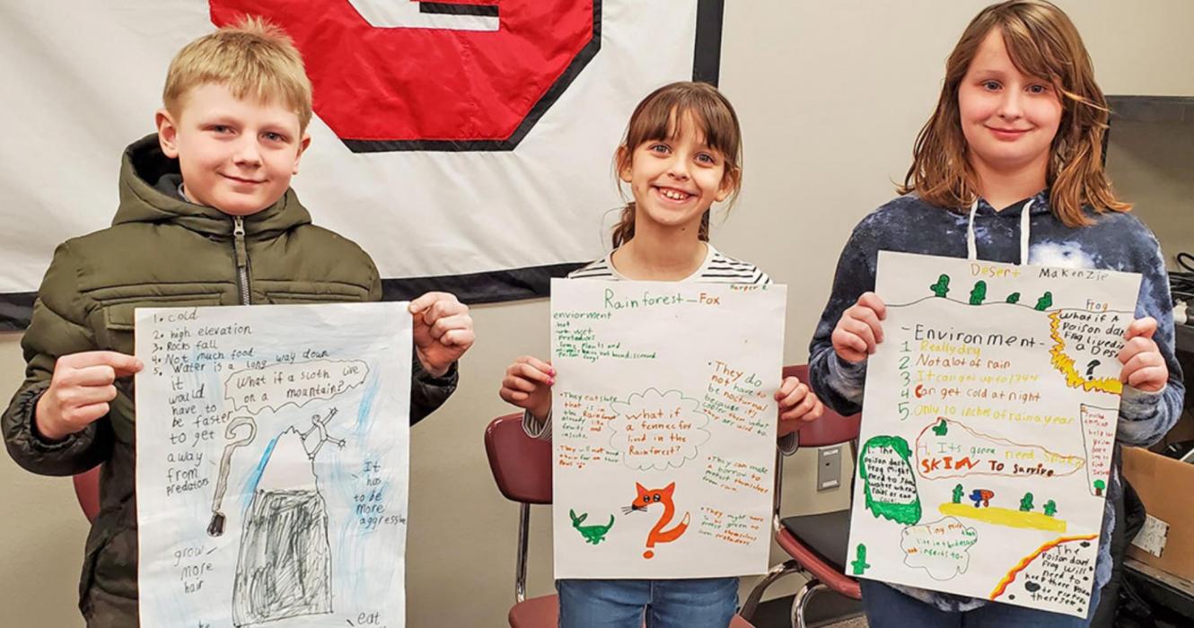 Third graders Emmett Shaffer, Makenzie Anderson, and Harper Rudy showed the posters that they made in science class to the school board, explaining what adaptations different animals would have to make if they were moved to a new habitat.