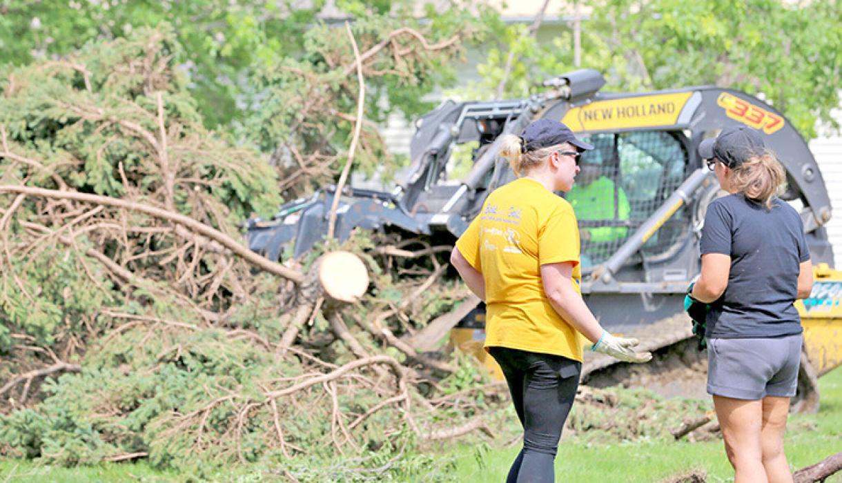 Sal Roseland, right, of Seneca, South Dakota, talks with Gov. Larry Rhoden as Rhoden operates Roseland’s skidsteer loader on June 29, 2026. Roseland drove to Highmore after severe storms to assist cleanup efforts. (Photo by Meghan O’Brien/South Dakota Searchlight)