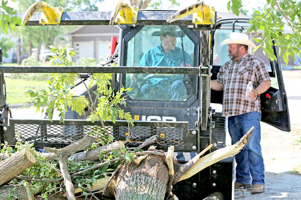 Matilyn Kerr, left, and sister Brittany Kerr watch as a skid-steer loader pulls a tree from Brittany Kerr’s yard in Highmore, South Dakota, on June 29, 2026, after a severe storm that morning. (Photo by Meghan O’Brien/South Dakota Searchlight)