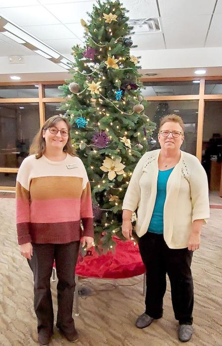 BankWest employees Michelle Birkeland, left, and Lea Schell, right, stand next to the Community Christmas Tree.