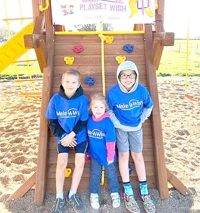Evie Tietgen and her brothers Josh (l) and Jason (r) stand in front of the climbing wall of her playset, her wish granted through Make-A-Wish.
