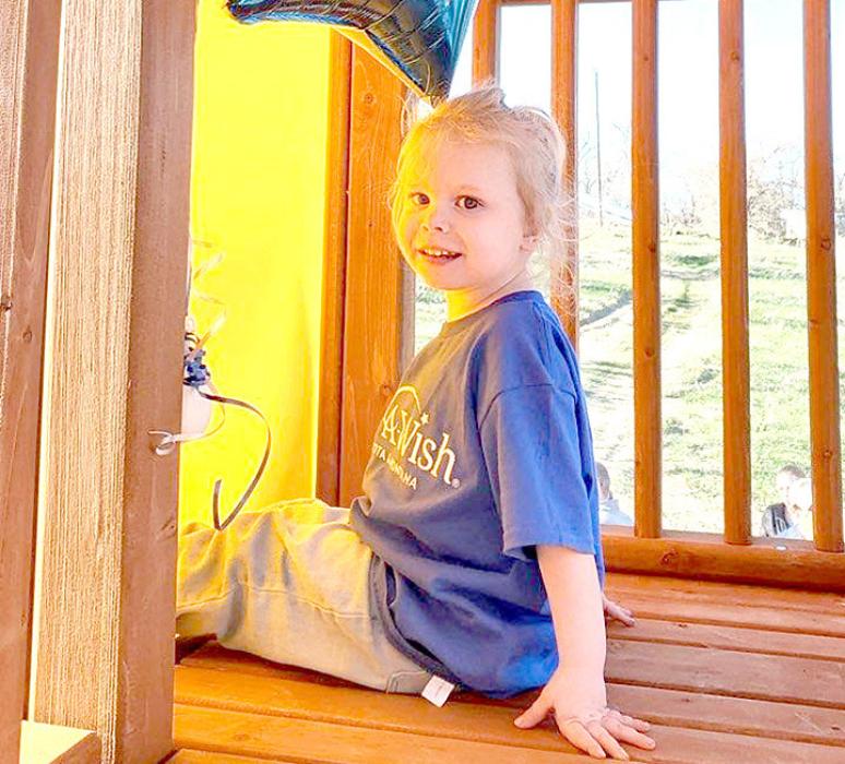 Evie sits at the top of one of the play set’s slides, her favorite feature, the day of her wish fulfillment celebration.
