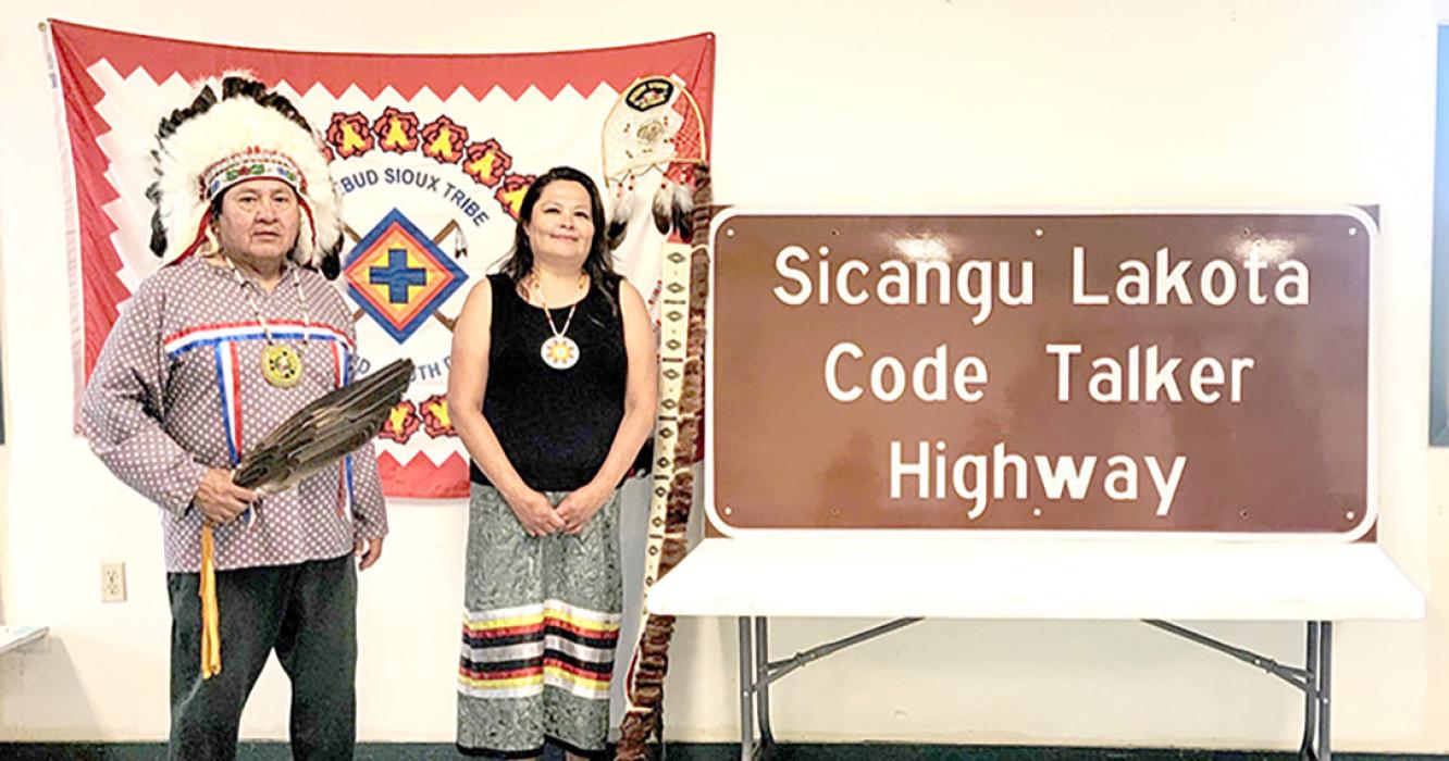 Willie Bearshield and Lisa White Pipe, descendants of Code Talker Charles White Pipe, stand next to the sign designating a 153-mile portion of US Highway 18 as Sicangu Lakota Code Talker Highway in honor of the many Lakota Code Talkers from South Dakota who served the US military in World War II.