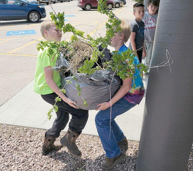 A couple fourth graders wrestle with a heavy, awkward bag of branches and refuse they cleaned up.