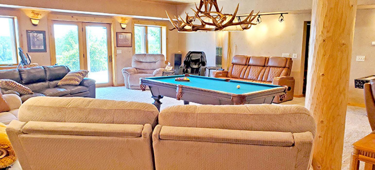 The basement has several amenities for guests, including a rec room with a pool table and large screen TV, exercise equipment, a massage chair, a theater room, laundry facilities, and a walkout to a patio with a hot tub and seating for up to 13.