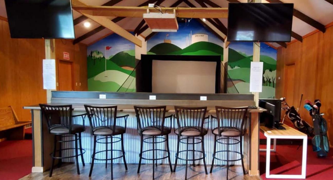 The bar overlooks the golf screen, providing seating as golfers wait their turn. Numerous outlets not only let customers charge their devices, but also come in handy for crockpots if the facility is used for a potluck or party.