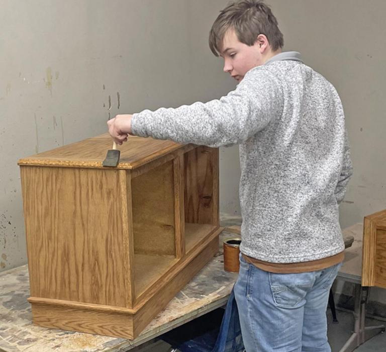 Jaden Graber applies a finish to a cabinet that he made in one of the shop classes. (Submitted photo)